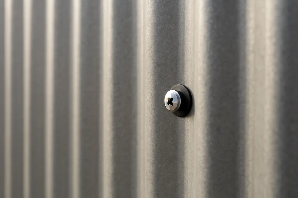 A close view of a plain corrugated metal wall panel with a screw and washer in the ridge — pole barn, Tyler. Illustrative example.